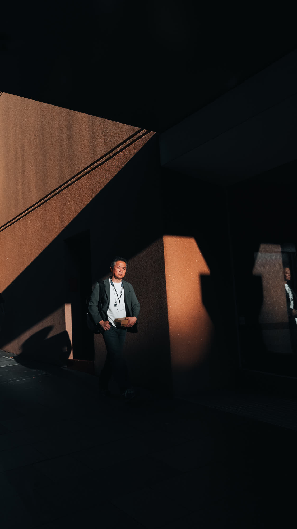 A man in a suit standing in a shaft of hard afternoon light