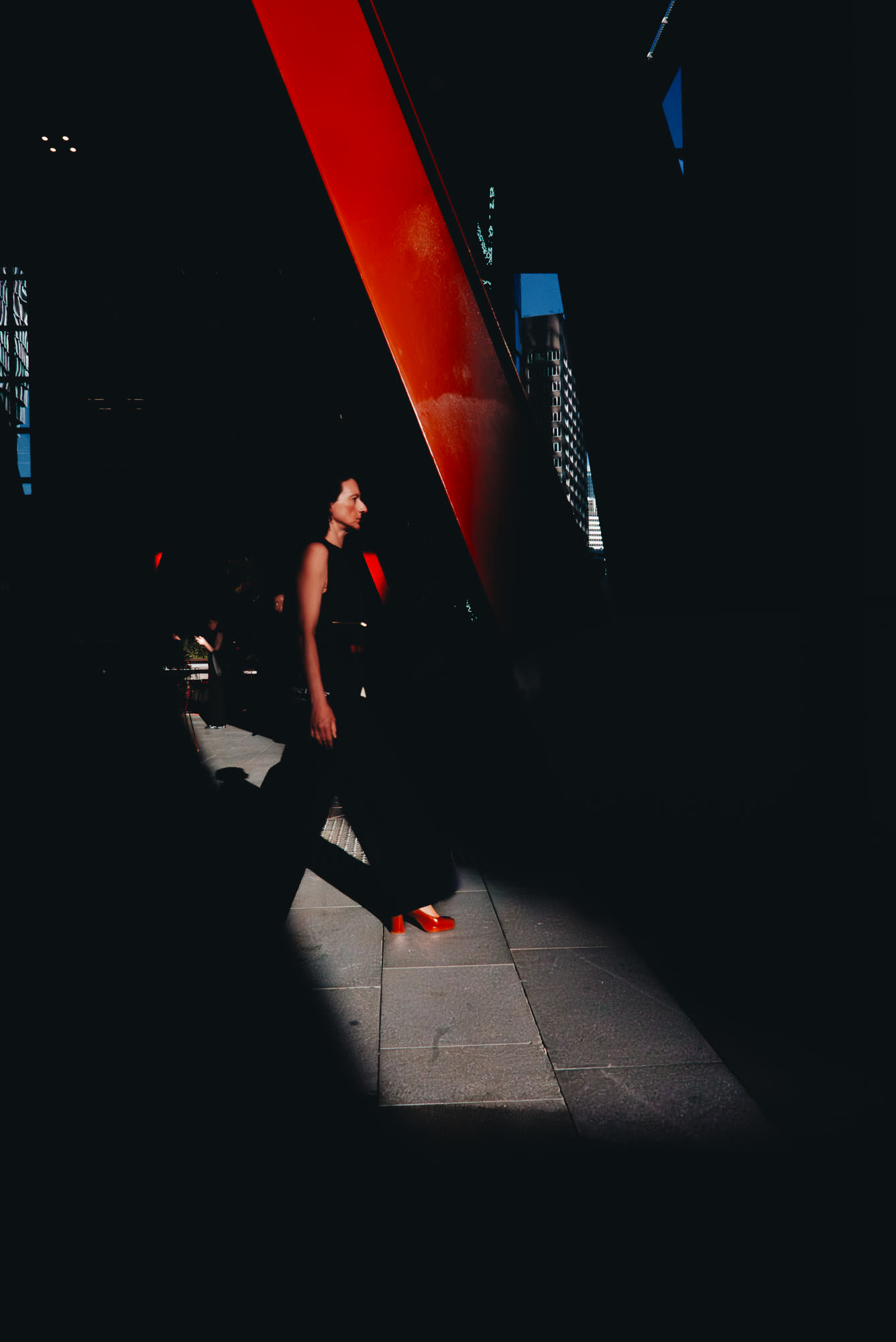 A woman walking past a red awning at night, red shoes catching the light