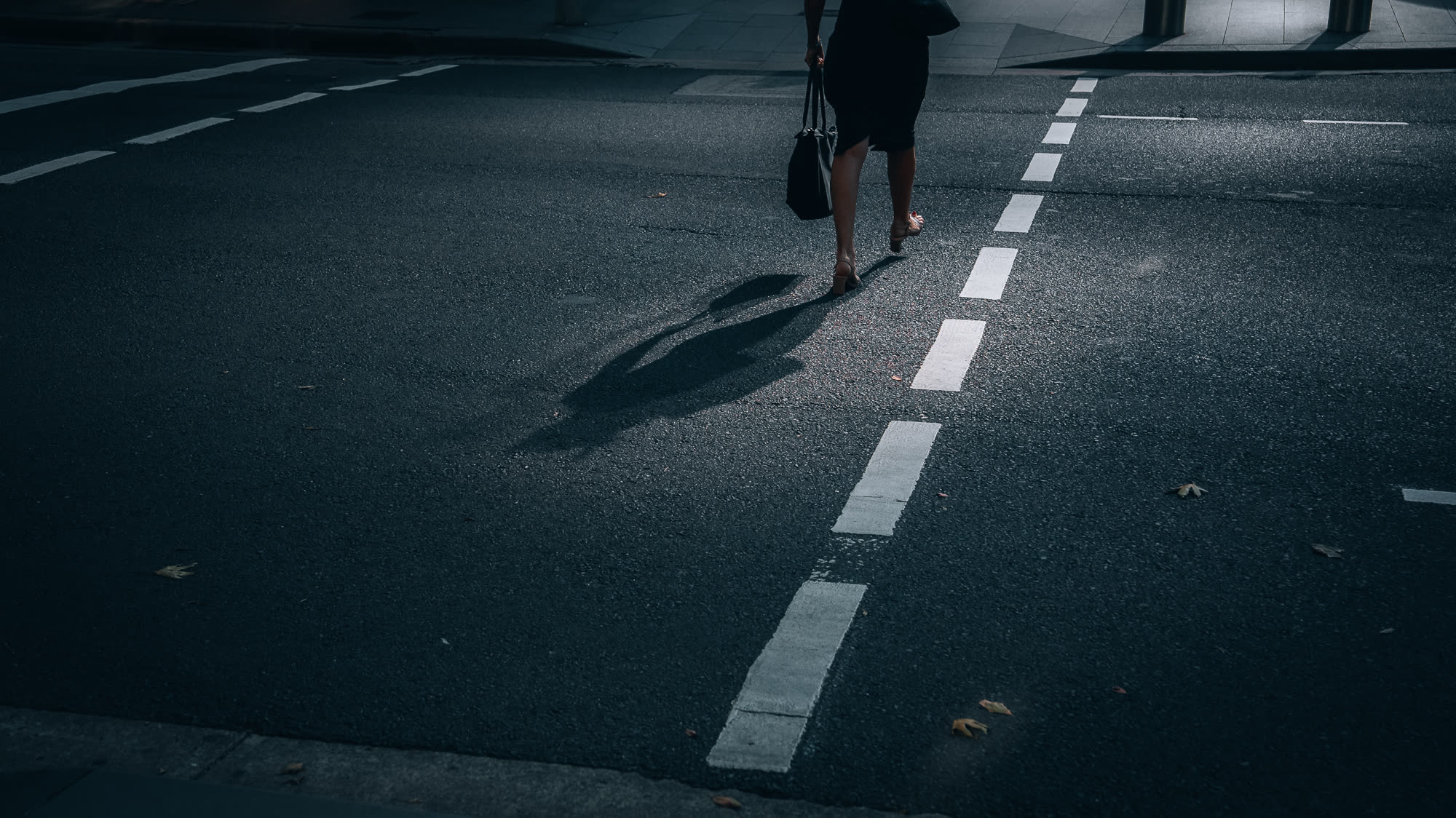 A lone figure crossing the road, long shadow on the asphalt